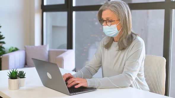 Seious Mature Grayhaired Businesswoman Wearing Mask in Modern Office Looks at the Camera