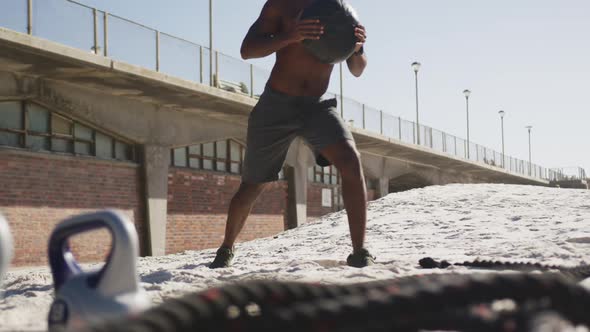 Focused african american man lifting ball, exercising outdoors on beach