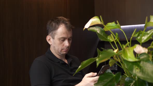 European Man Sitting in Cafe with Cup of Coffee and Watch the News on His Phone