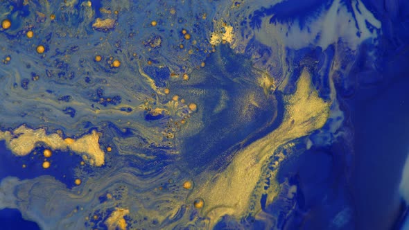 Process of mixing liquid blue and gold paint. Floating spots of golden paint mix with blue color. alt
