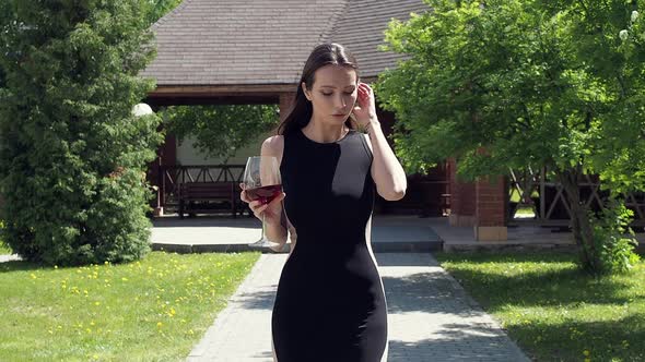 Elegant Woman with Glass of Wine Walking in Garden of Mansion