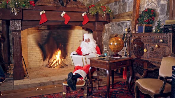 Santa Claus is sitting in specially decorated room and looking at the book.