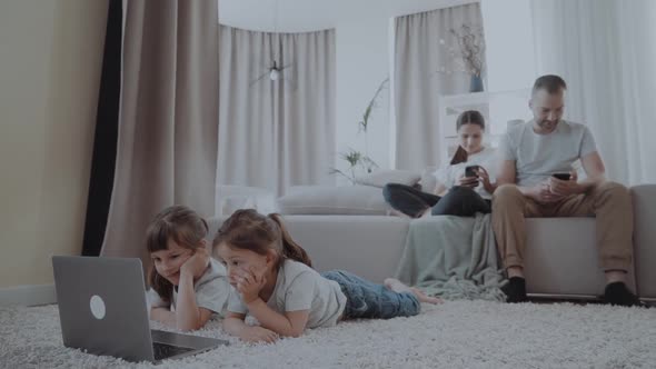 Children Watch Videos on a Laptop While Parents Use the Phone