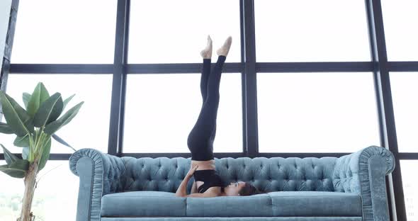 Sexy Girl Doing Exercises While Lying on Blue Sofa. Active Athletic Woman Exercising at Home Lazy