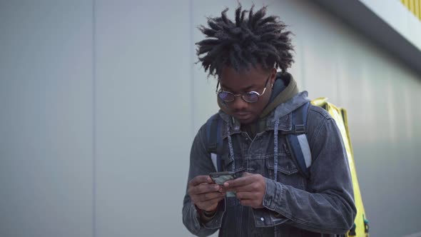 Concentrated African American Young Man Checking Online Map in Smartphone and Leaving with Yellow