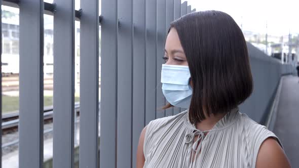 Woman looking through metal fence with a hygienic respirator mask over her nose and mouth. Slow Moti