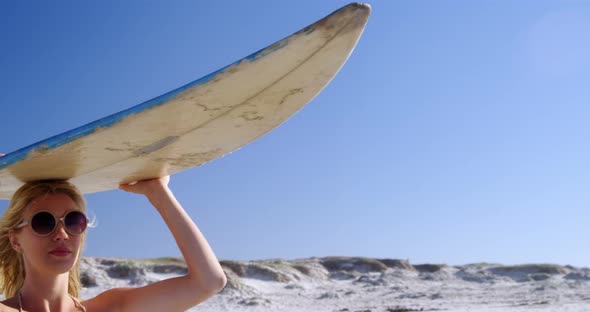 Young woman carrying surfboard on head at beach