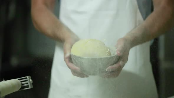 Baker With Apron Tossing Dough With Flour On A Stainless Bowl. - medium shot