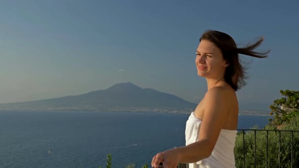 Young Woman Stands on a Balcony with a Beautiful View of the Sea and Mountains