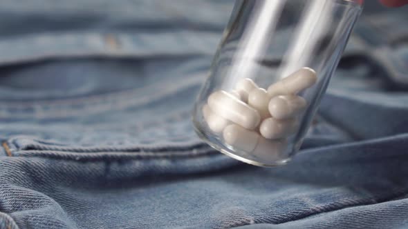 bottle with white capsules shakes over blue denim clothes. 