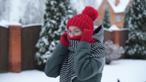 A young woman wrapped in a hat and scarf walks along a snowy street