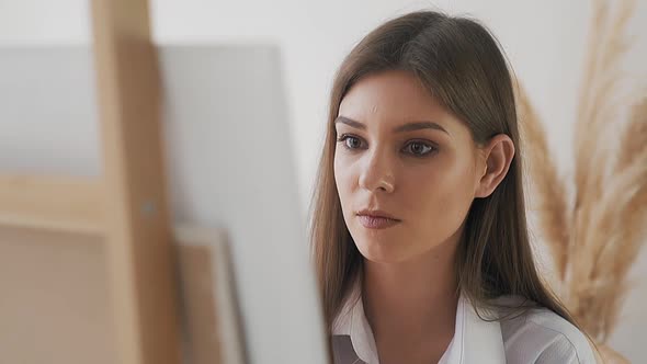 Woman Art Student Looks at Canvas with New Picture on Easel