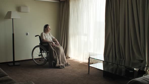 Senior Woman Sit on Wheelchair and Looks Through the Window