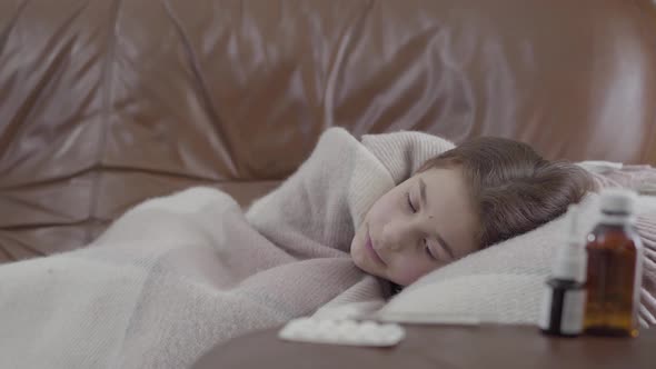 Portrait Teenage Ill Girl Lying on the Sofa Covered with a Blanket at Home, She Is Cold. Nasal Spray