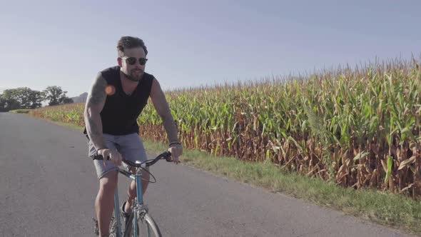 Cheerful man riding bicycle along rural field