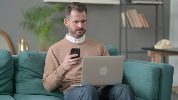 Man with Laptop Using Smartphone on Sofa