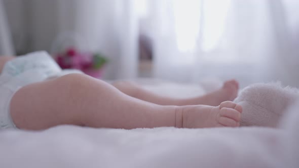 Side View Little Newborn Baby Legs Moving As Child Lying on Cozy White Bed