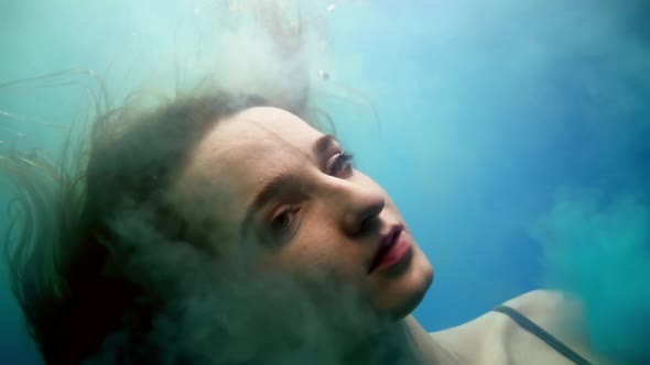 Enigmatic Woman is Diving Into Depth of Pool or Magic Lake Closeup of Face in Clouds of Smoke