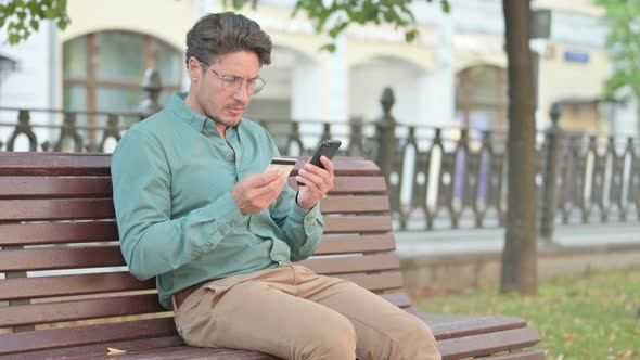 Man making Online Payment on Smartphone in Park Bench