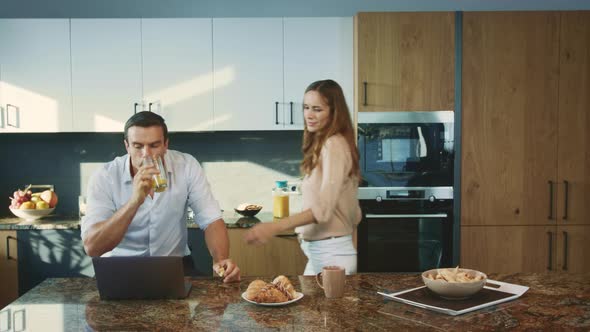 Concentrated Man Working at Luxury Kitchen. Smiling Wife Talking with Husband