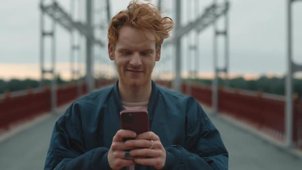 Handsome Hipster with Red Hair Using Smartphone Outdoors