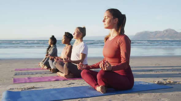 Group of diverse female friends meditating at the beach