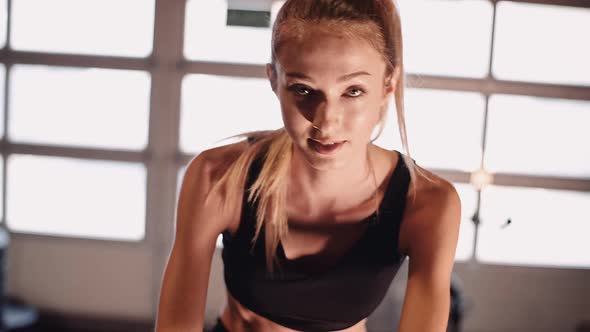 Young Fit Sporty Blone Girl Exercising on a Bike at Gym