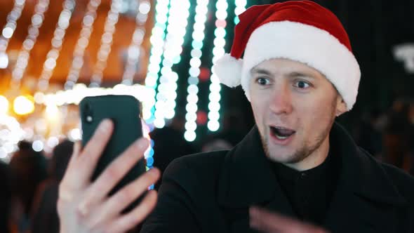 Cheerful Man Taking Video Call From Friends on Mobile Phone, Dressed in Christmas Hat. Christmas