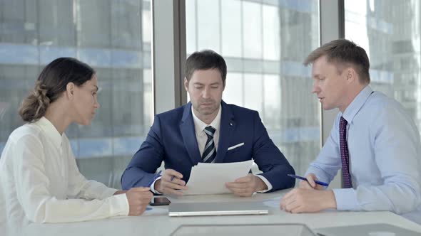 Middle Aged Businessman Having Reading Documents with His Assistants in Boardroom