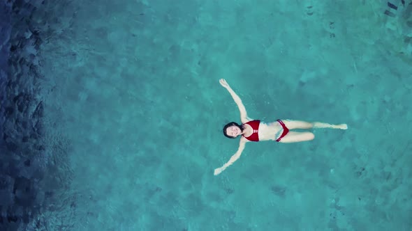 Young Woman in Red Bikini Lays on Blue Water Pool