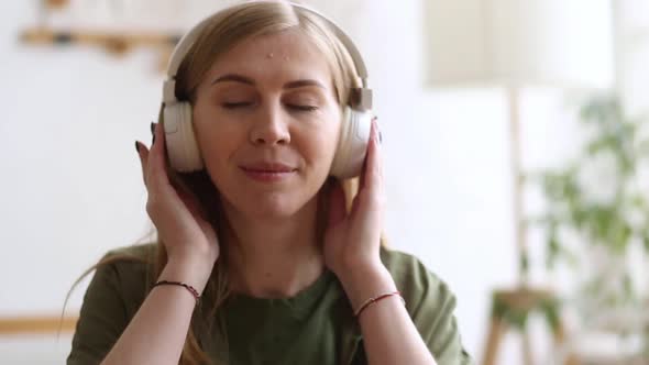 Cute Blonde Closeup Listening to Music with White Headphones in the Room and Dancing