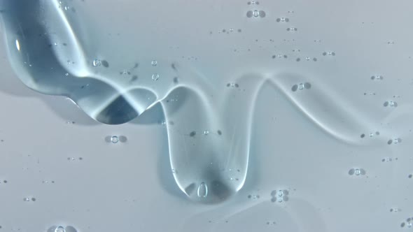 Transparent Blue Cosmetic Gel Fluid with Bubbles Flowing Down on a White Surface