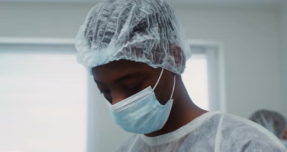 A Young AfricanAmerican Doctor with Medical Cap and Mask Looks Into Camera