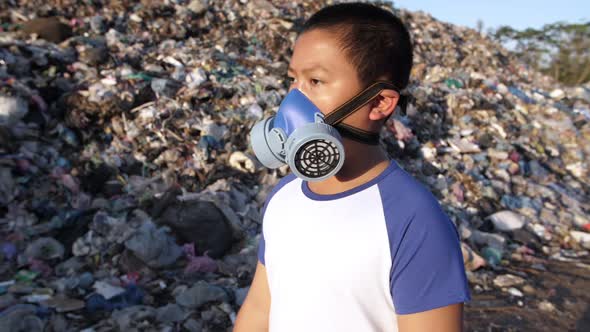 Young Boy Wearing Pollution Mask Walking Near Garbage Pile alt