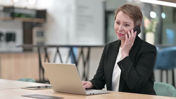 Old Businesswoman with Laptop Talking on Smartphone 