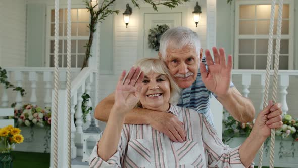 Senior Elderly Couple in Front Yard at Home. Man Hugging Woman. Happy Mature Family Waving Hands