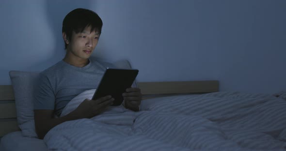 Asian man watching on tablet on bed 