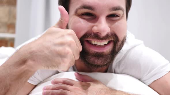 Thumbs Up By Happy Beard Man Lying in Bed on Stomach