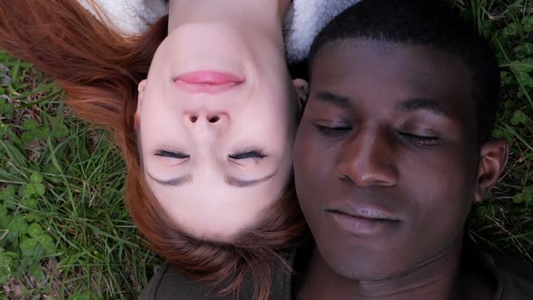 Mixed love concept.Interracial young couple lying on lawn opening eyes closed