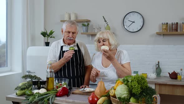 Senior Couple in Kitchen. Elderly Grandmother and Grandfather Eating Raw Broccoli and Cauliflower