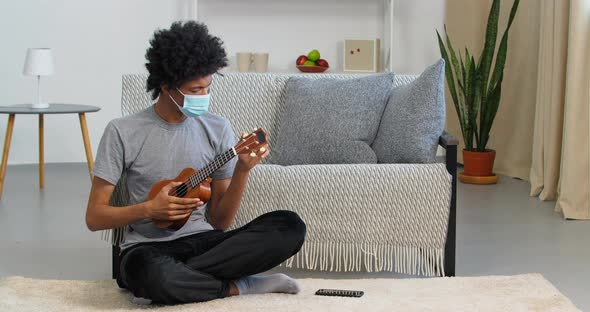 Afro American Guy Sick Man Musician Wears Casual Clothes and Medical Face Mask Sitting on Floor