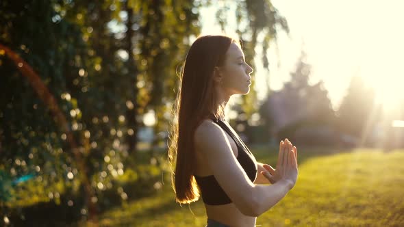 Tracking shot of attractive young woman practicing yoga performing namaste pose, breathing deeply.