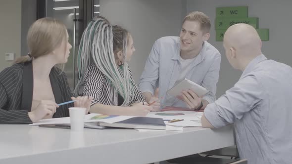 Four Cheerful Young Colleagues Talking and Giving Highfive in Office