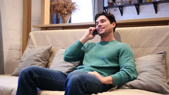 Young Man Talking on Phone Attending Phone Call Sitting at Home