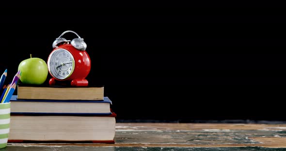 Apple and alarm clock on book stack with color pencils on table