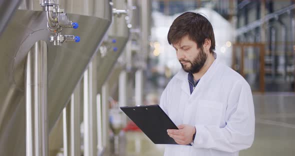 Man in White Lab Coat Looking at Equipment Gauge and Entering Data in Tablet