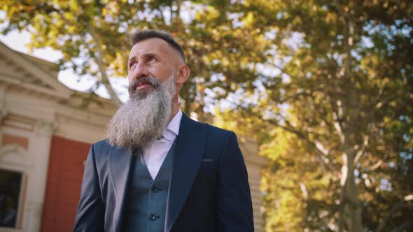 Portrait of Handsome Bearded Mature Man in Suit Outdoorsin Park During Sunny Day
