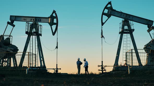 Technicians Are Talking Between Two Oil Pumping Units. Oil Well, Crude Oil, Drilling Rig, Oil Field