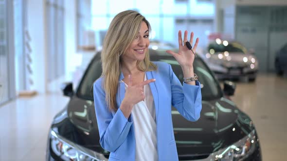 Zoom in to Happy Woman Showing Car Key Looking at Camera Standing in Dealership Indoors