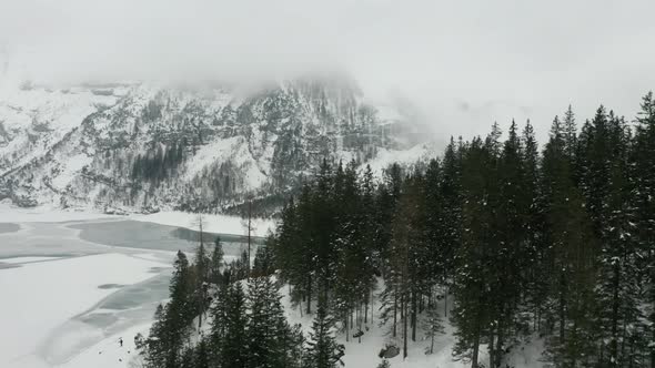 Flying over tree tops with a snow covered landscape and frozen lake in the background